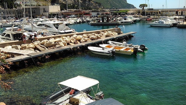 A marina with various boats docked, a rocky shoreline, and buildings in the background. - Unique panorama with the best view of Cassis (Cassis)