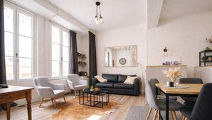 Un salon moderne comprenant un canapé, des fauteuils, une table à manger, une table basse, un tapis et un grand miroir.