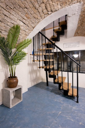 Una escalera con barandillas negras y escalones de madera, una planta en maceta y un cartel que indica un teatro.