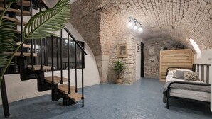 Une pièce avec un escalier, un lit, une plante et un mur en briques.
