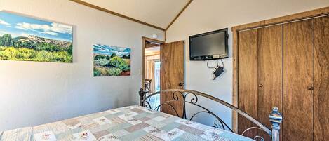 A bedroom with a bed, a wooden wardrobe, a television, and two landscape paintings on the wall.