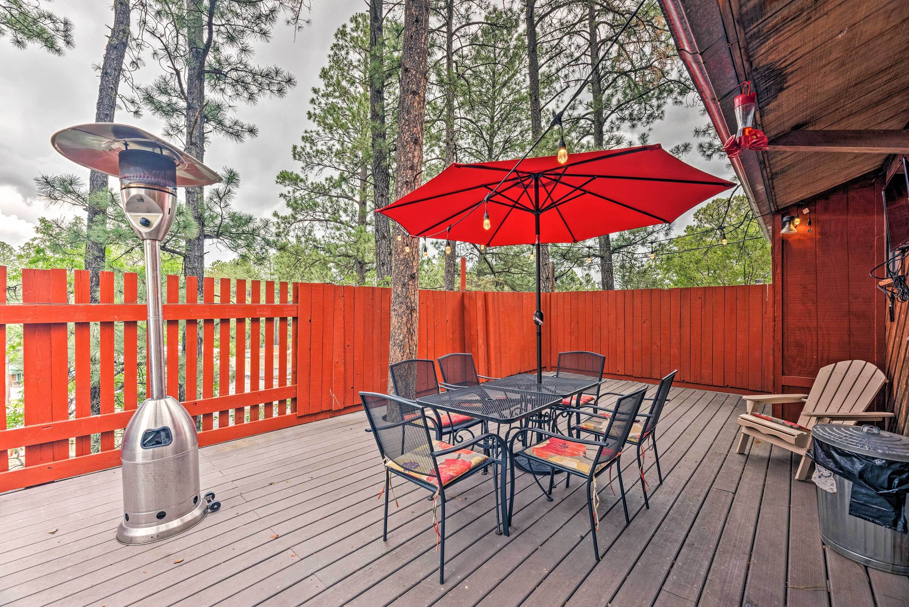 An outdoor deck with a metal table and chairs, a red umbrella, and a metal heater.