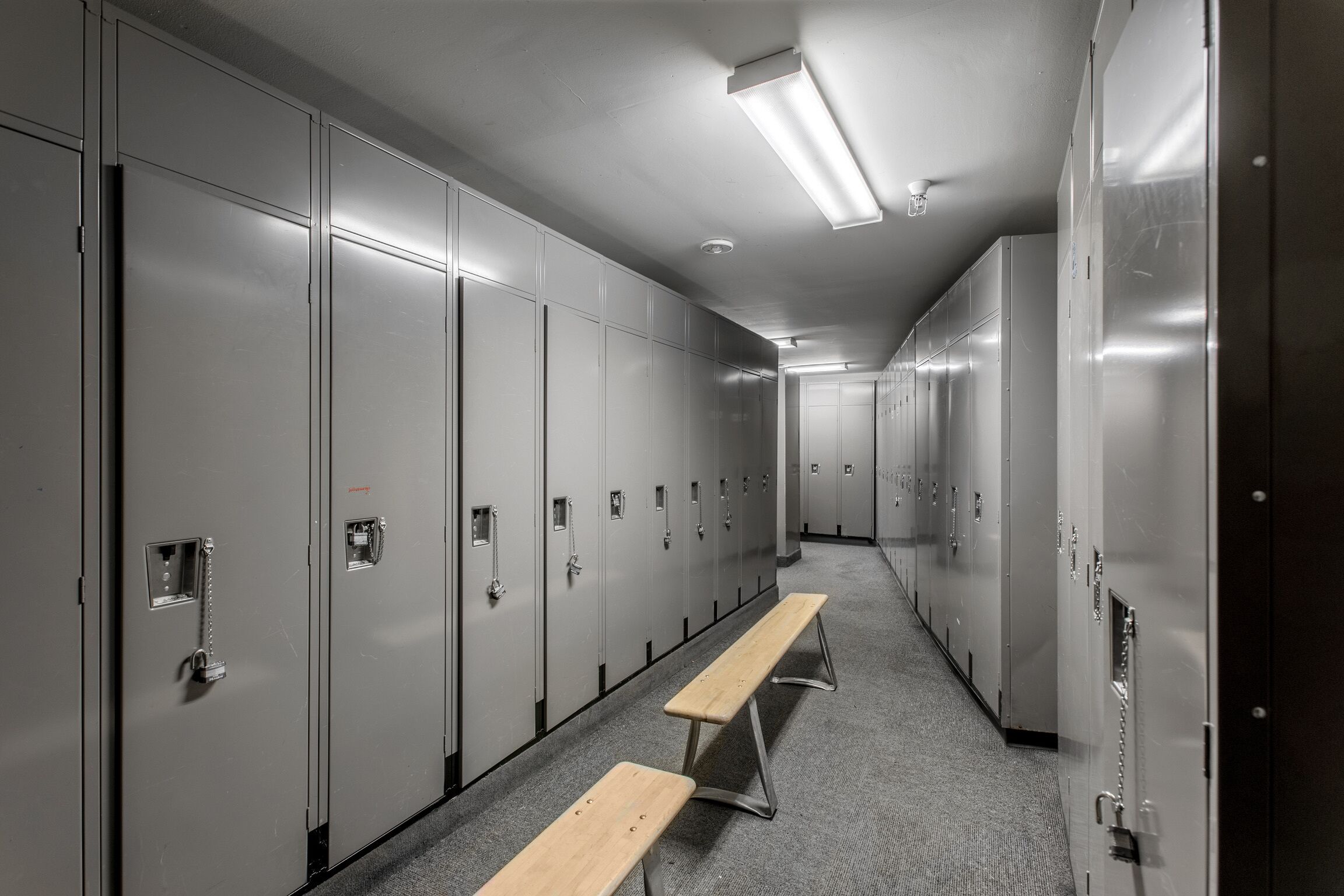 A locker room with metal lockers, benches, and fluorescent lighting.