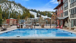 Une piscine avec des chaises longues et vue sur une piste de ski.