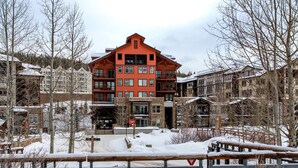 Un immeuble à plusieurs étages, doté d’une façade rouge, entouré d’arbres couverts de neige et d’une clôture en bois.