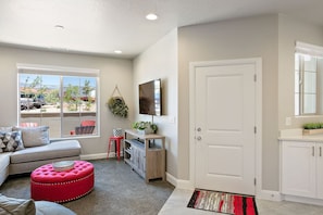 A living room with a sectional sofa, a red ottoman, a TV, and a wooden cabinet.