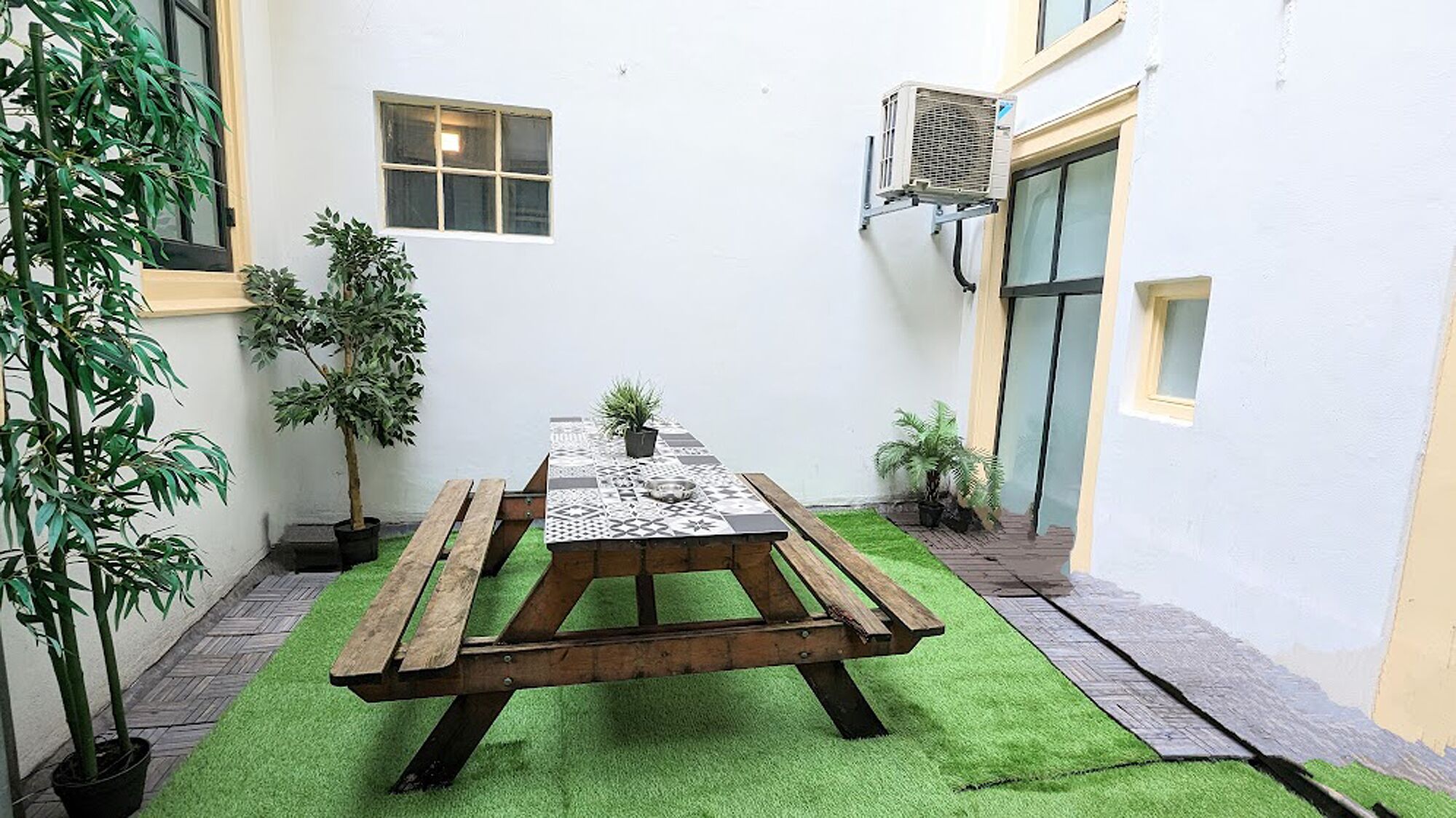 A courtyard with a wooden picnic table, potted plants, and a small window.