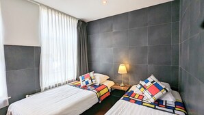 A hotel room with two beds, a nightstand, a lamp, and a window with curtains. - 3 Bedrooms Apartment in Amsterdam City Center (Amsterdam-Centrum)