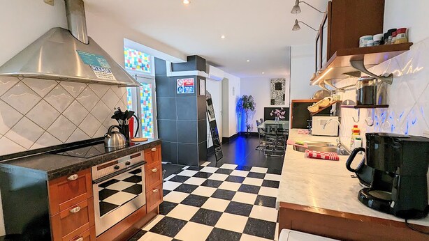 A modern kitchen with a black and white checkered floor, stainless steel appliances, and a large window with a colorful view. - 3 Bedrooms Apartment in Amsterdam City Center (Amsterdam-Centrum)