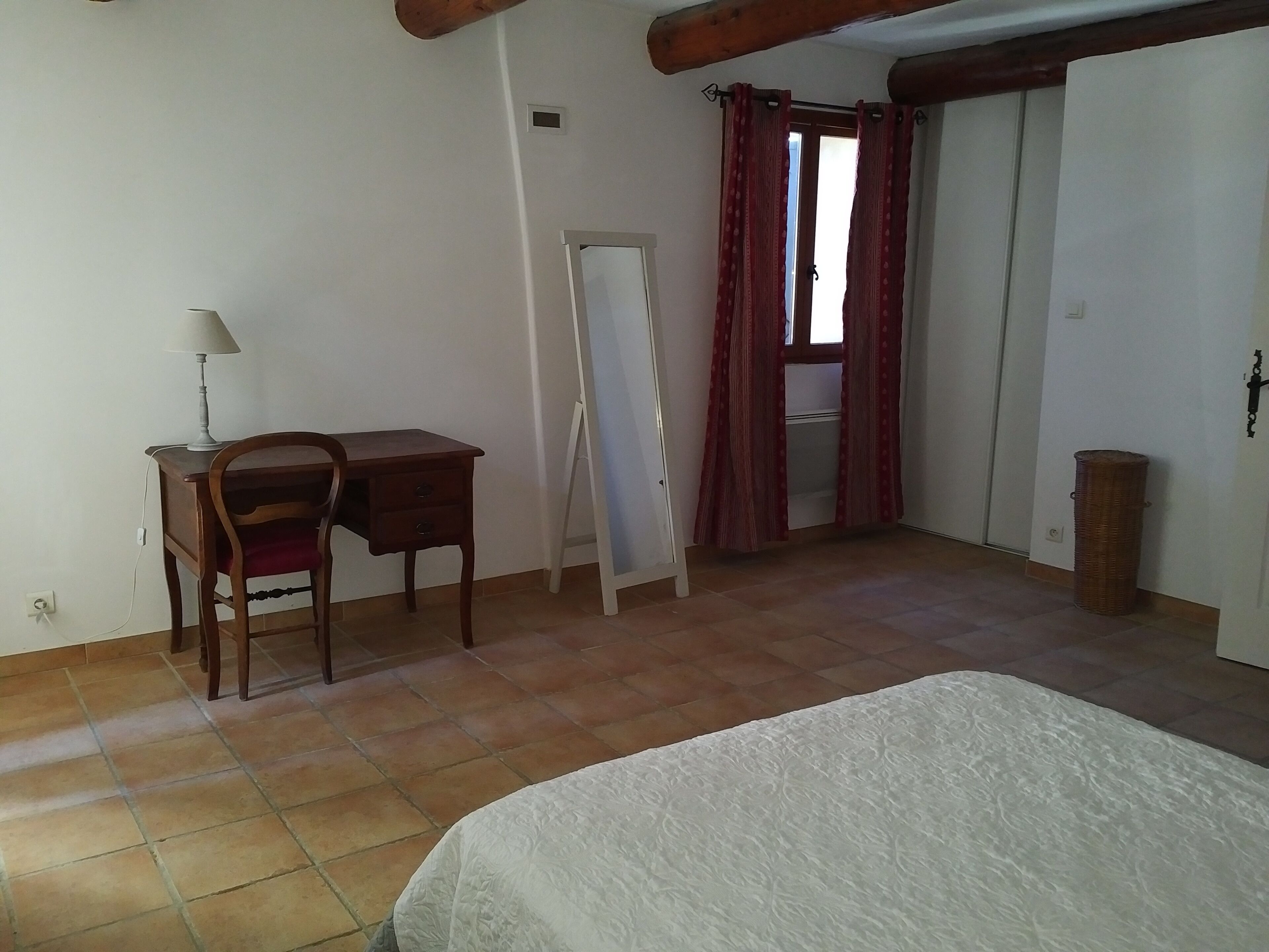 Une chambre à coucher avec un lit, un bureau, une chaise, un miroir et une porte.