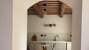 Een keuken met een eethoek, voorzien van een betegelde vloer, houten balken en een hangende lamp.