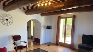 Een woonkamer met een houten plafond, een bank, een salontafel, een televisie en uitzicht door een glazen deur.