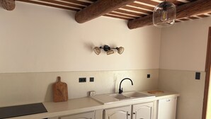 Een keuken met een wit aanrecht, een spoelbak, een houten snijplank en een eethoek met een tafel en stoelen.