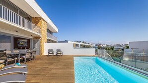 Un área de piscina en la azotea con terraza de madera, sillones de descanso y vistas a la ciudad.