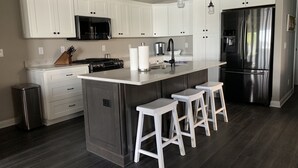 A modern kitchen with white cabinets, stainless steel appliances, and a central island with bar stools. - NEW Lake James, Indiana Waterfront Rental (Angola)
