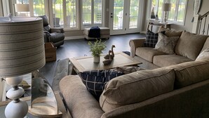 A spacious living room with a large window overlooking a lake, a comfortable sofa, a coffee table, and a lamp. - NEW Lake James, Indiana Waterfront Rental (Angola)