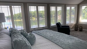 A bedroom with a large bed, multiple windows, and a view of a lake. - NEW Lake James, Indiana Waterfront Rental (Angola)