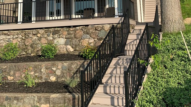 A two-story house with a stone foundation, a balcony with a black railing, and a staircase leading to the second floor. - NEW Lake James, Indiana Waterfront Rental (Angola)
