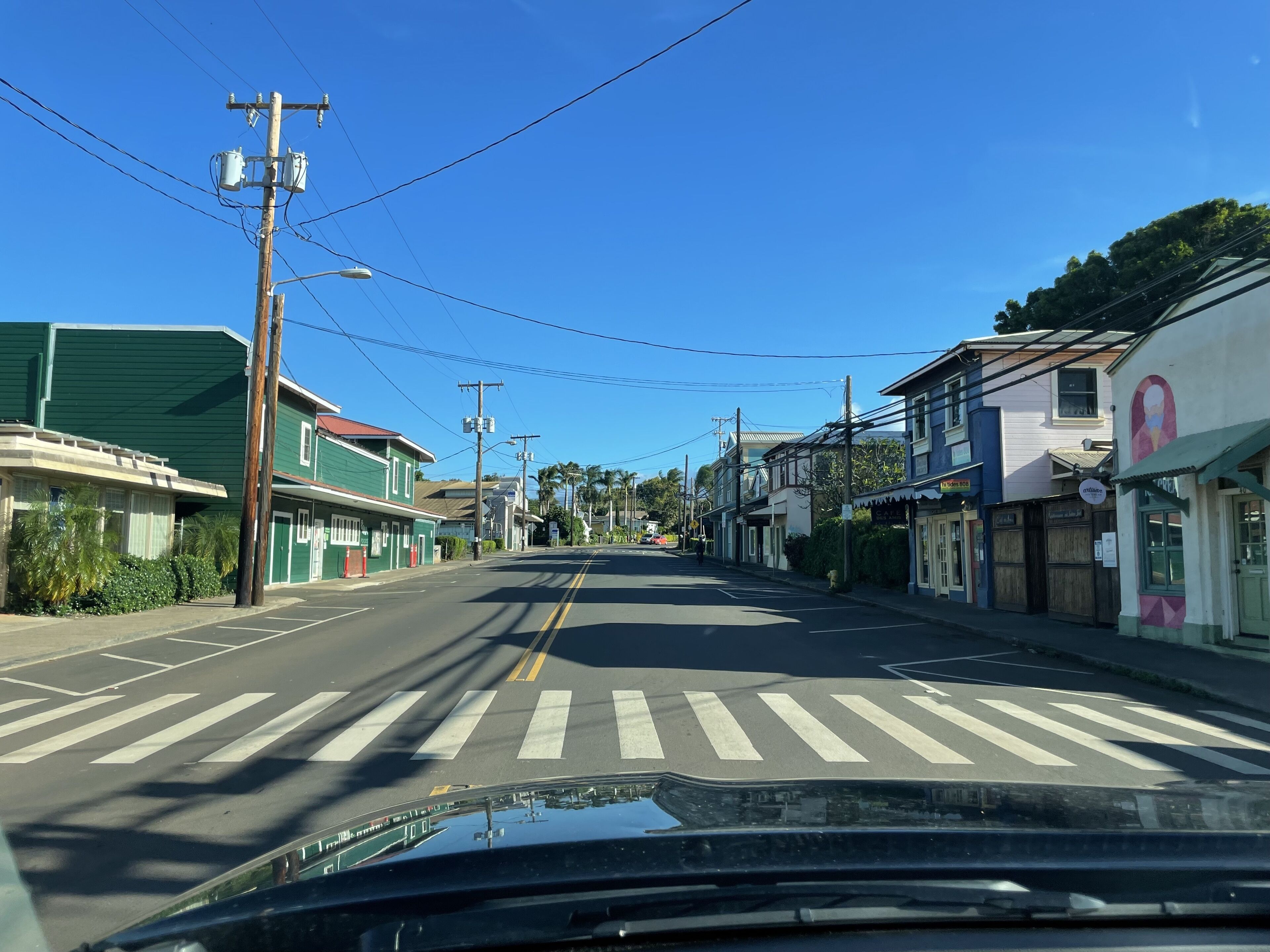A street view with buildings on both sides, a crosswalk, and utility poles with wires.