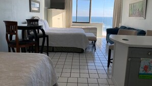 Habitación de hotel con dos camas, un escritorio, una silla, un televisor y vista al océano.