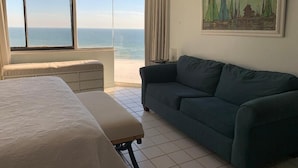 Una habitación con una cama, un sofá verde, una ventana con vista al mar y un cuadro en la pared.