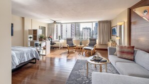 A modern hotel room with a large window, a bed, a sofa, a desk, and two chairs. - Spacious renovated studio in downtown Waikiki (Honolulu)
