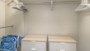 A bathroom with a white tiled wall, a towel rack, a shower curtain rod, and a blue backpack on a cart. - Spacious renovated studio in downtown Waikiki (Honolulu)