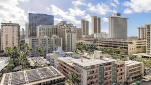 A high-rise urban area with multiple buildings, including a prominent blue glass building, surrounded by palm trees and other greenery. - Spacious renovated studio in downtown Waikiki (Honolulu)