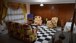 Uma sala de estar com piso xadrez, dois poltronas estampadas, um sofá, uma televisão e um armário de madeira.