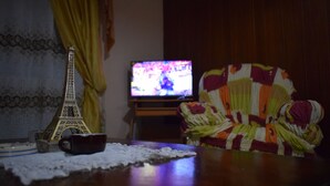 Uma pequena réplica da Torre Eiffel, uma televisão e uma cadeira colorida em um quarto com pouca luz.