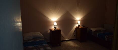 A dimly lit room with two beds, each with a bedside table and lamp.