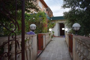 A stone pathway leading to a building entrance, flanked by decorative metal railings and potted plants. - La Casa  Skikda Jeandarc (Skikda)