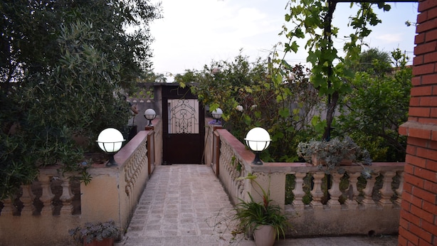 Uma escadaria de pedra leva a um portão com plantas em vasos e luminárias na parede.