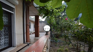 Área externa coberta com um banco de madeira, uma coluna de tijolos e um vaso com planta.