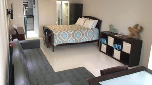 Een moderne slaapkamer met een bed, een bureau, een stoel en een sofa. Er is een plafondventilator en een plank met decoratieve objecten.