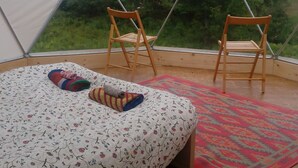 Une pièce aménagée avec une tente, un lit, deux chaises en bois, une couvre-lit à motifs et un tapis rouge.