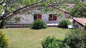 Ein Haus mit rotem Ziegeldach, weißer Fassade und einem kleinen Vorgarten mit Rasen und Büschen.