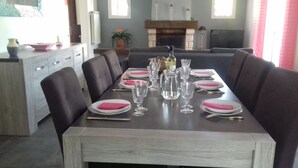 Ein Esszimmer mit einem langen Tisch, gedeckt für sechs Personen, mit dunklen Polsterstühlen, weißen Tellern, rosa Servietten und klaren Gläsern.