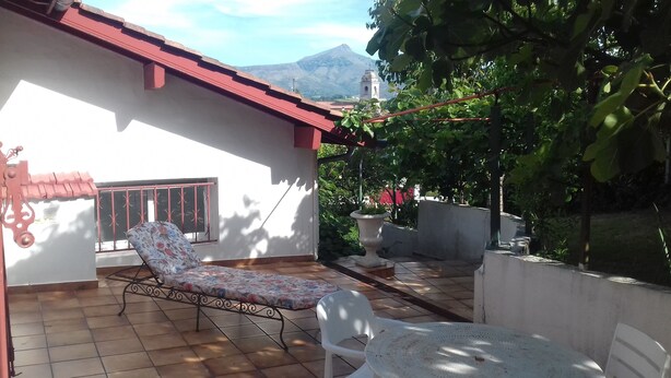 Eine Terrasse mit Liegestuhl, Tisch und Stühlen, einem Blumentopf und Blick auf einen Berg.