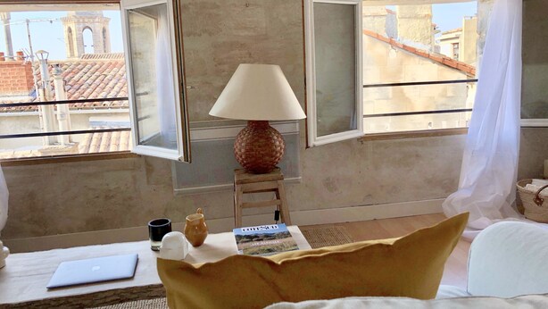 A hotel room with a bed, a table with a laptop, a lamp, and a window with a view of buildings.