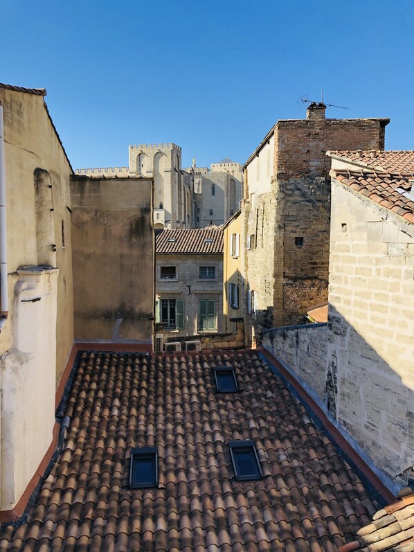 Une ruelle étroite, avec un toit recouvert de tuiles, des bâtiments en pierre et, au fond, une structure qui ressemble à un château.