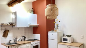 A compact kitchen with white cabinets, a stove, an oven, a microwave, and a hanging rattan light fixture.