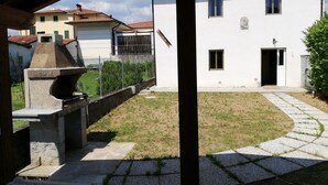 A courtyard with a stone pathway leading to a white building with a door and windows. - House -Mario- Single House CIN: IT046011C2K2ZAZUEE (Piano di Coreglia)