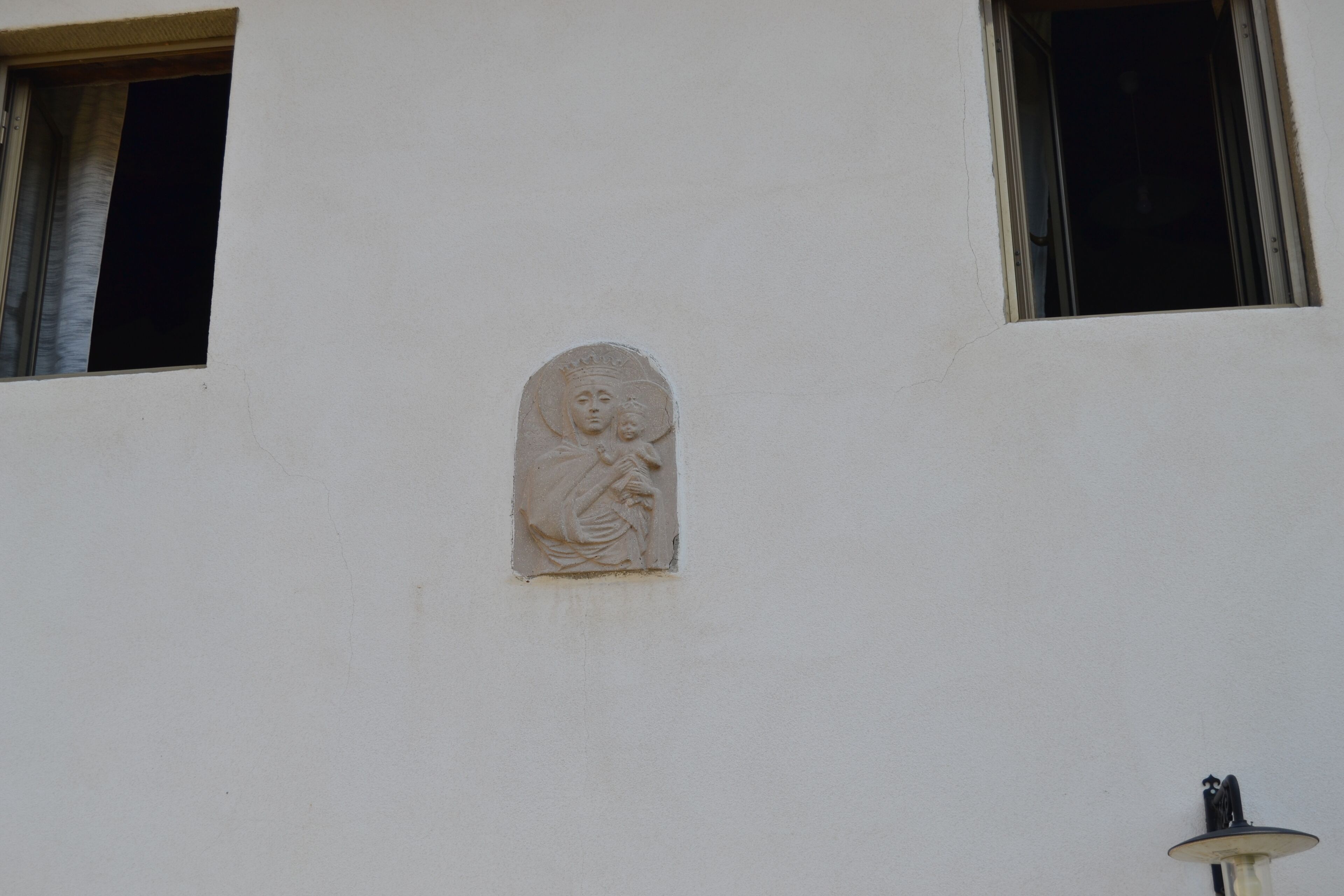 Fachada de edificio con un relieve de una figura, una ventana y una lámpara.