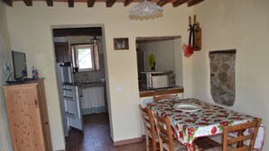 A dining area with a table set for four, wooden chairs, and a kitchen in the background. - House -Mario- Single House CIN: IT046011C2K2ZAZUEE (Piano di Coreglia)