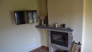 A living room with a fireplace, a flat-screen TV mounted on the wall, and a small shelf with decorative items. - House -Mario- Single House CIN: IT046011C2K2ZAZUEE (Piano di Coreglia)