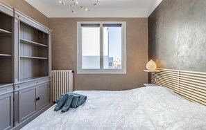 Ein Schlafzimmer mit Bett, Kleiderschrank, Heizkörper und Fenster mit Blick auf Gebäude.