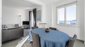 Una sala de estar moderna con un sofá gris, un televisor y una mesa de comedor con sillas de mimbre.