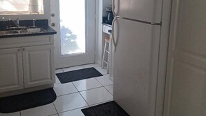 Uma cozinha com armários brancos, uma geladeira e uma janela com persianas.