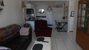 Um espaço de estar compacto com um sofá, uma poltrona vermelha, uma mesa pequena e uma área de cozinha ao fundo.